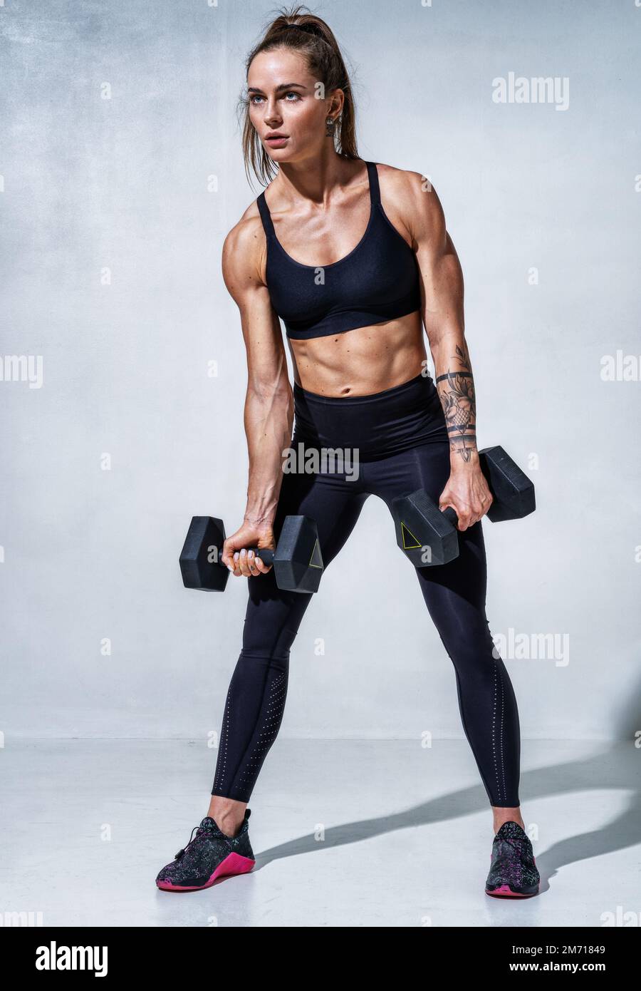 Sporty woman resting after workout with dumbbells. Photo of woman with good physique on grey background. Strength and motivation. Full length Stock Photo