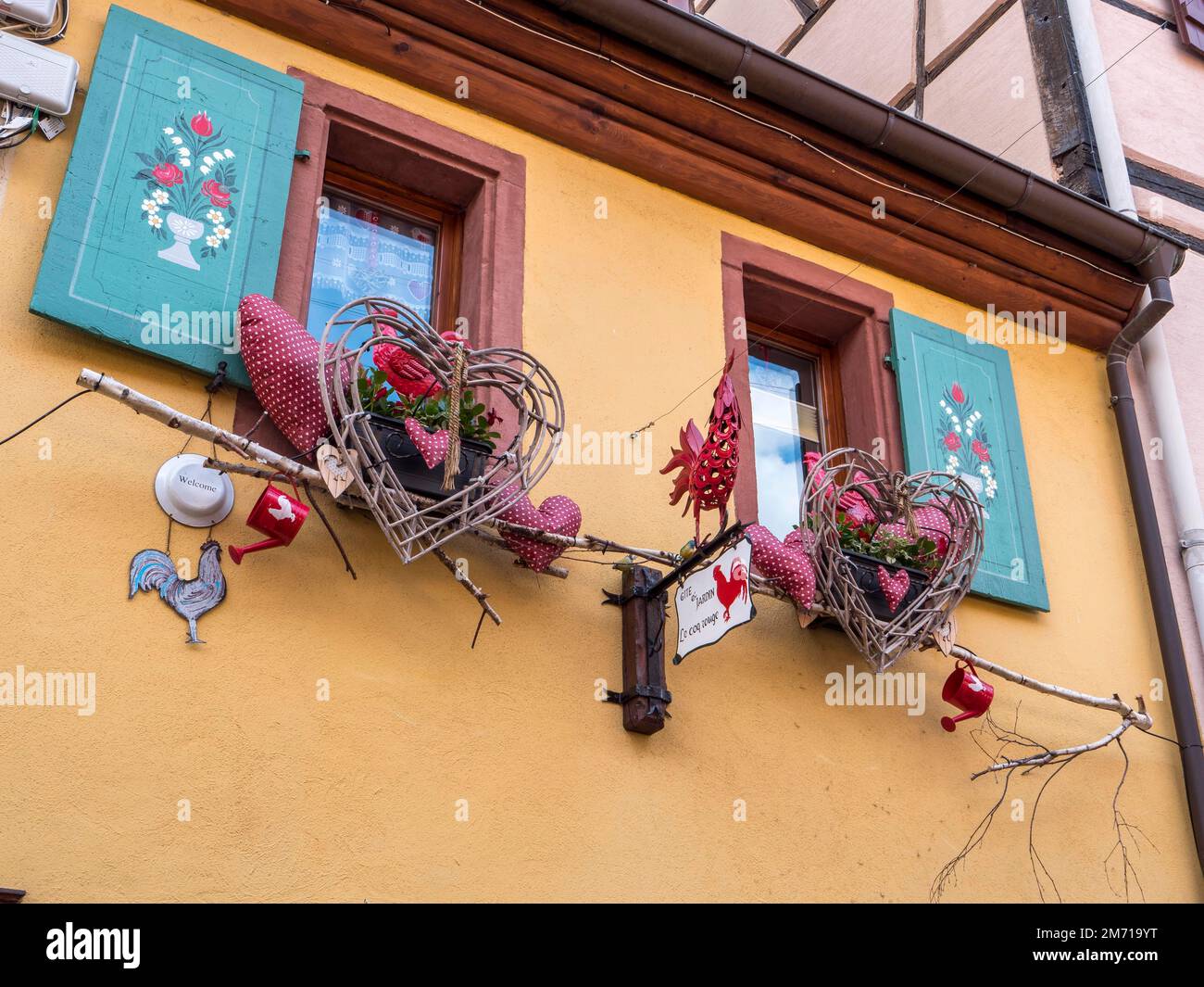 The windows of the yellow building are decorated with colourful hearts, Eguisheim, Grand Est, Haut-Rhin, Alsace, Alsace, France Stock Photo