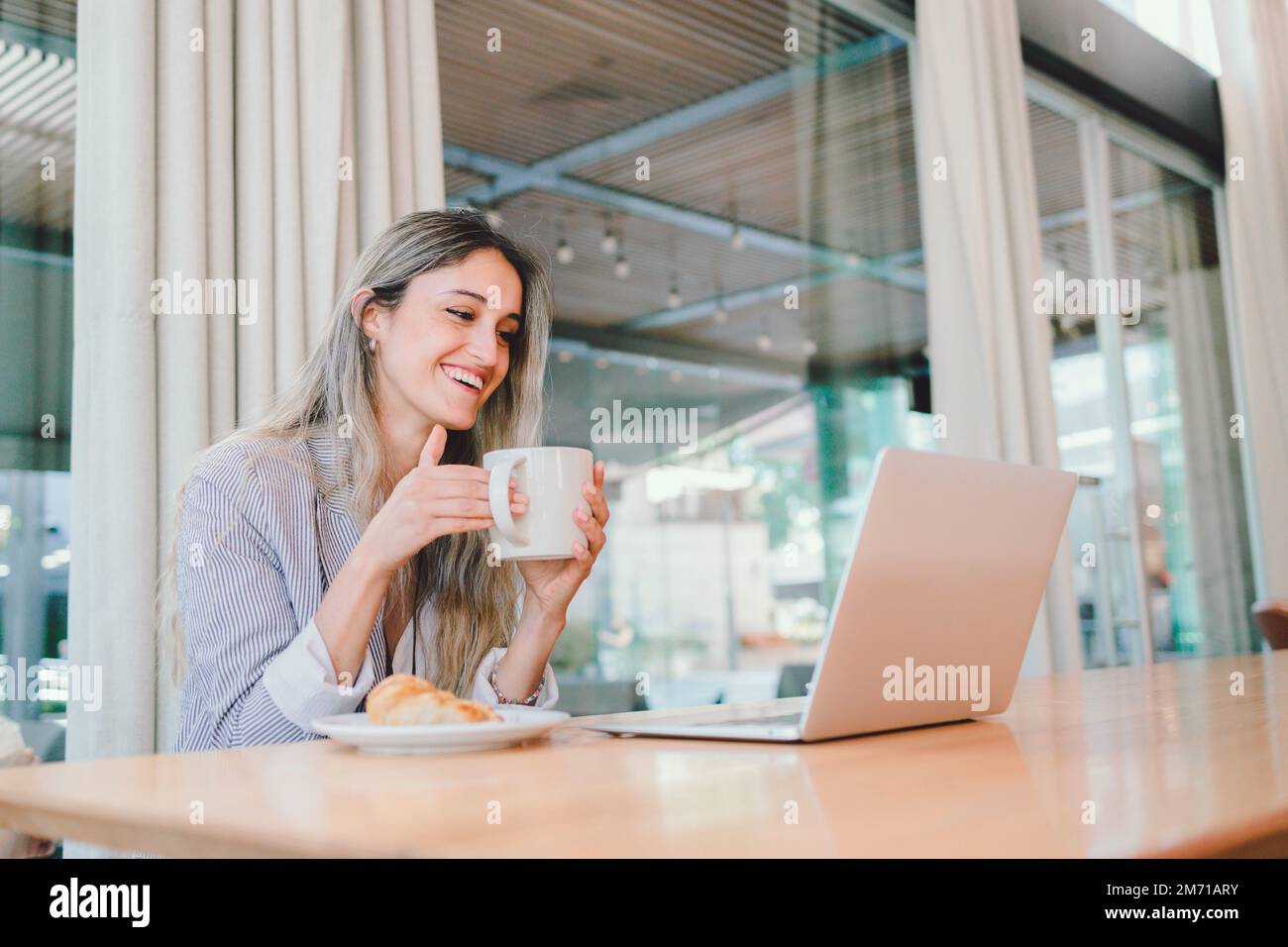 Young woman having a good time, using her laptop, drinking coffee from a mug. Habits to fight depression  Stock Photo