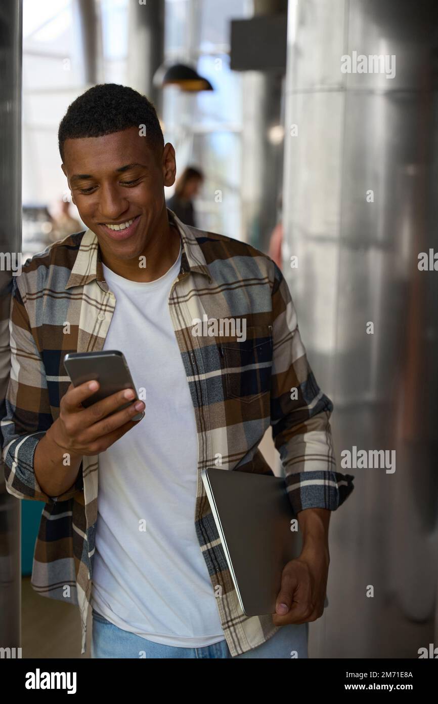 Smiling guy reading the message on phone while holding laptop Stock Photo