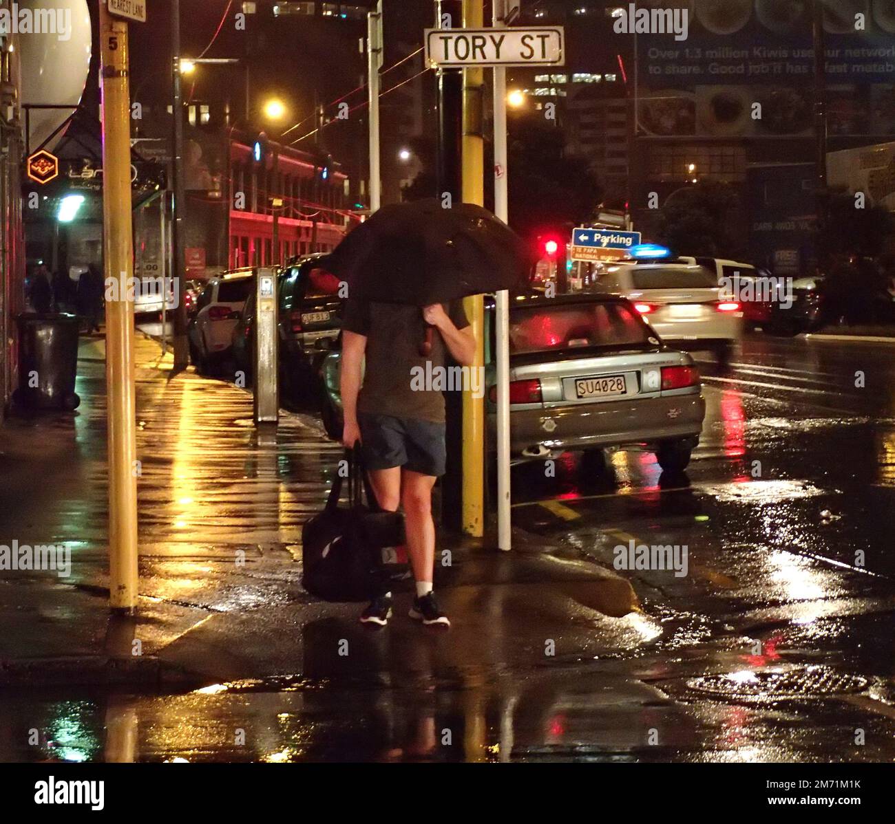 Man in shorts and tshirt waiting at the cross signal on a cold and wet winter night in Wellington NZ Stock Photo