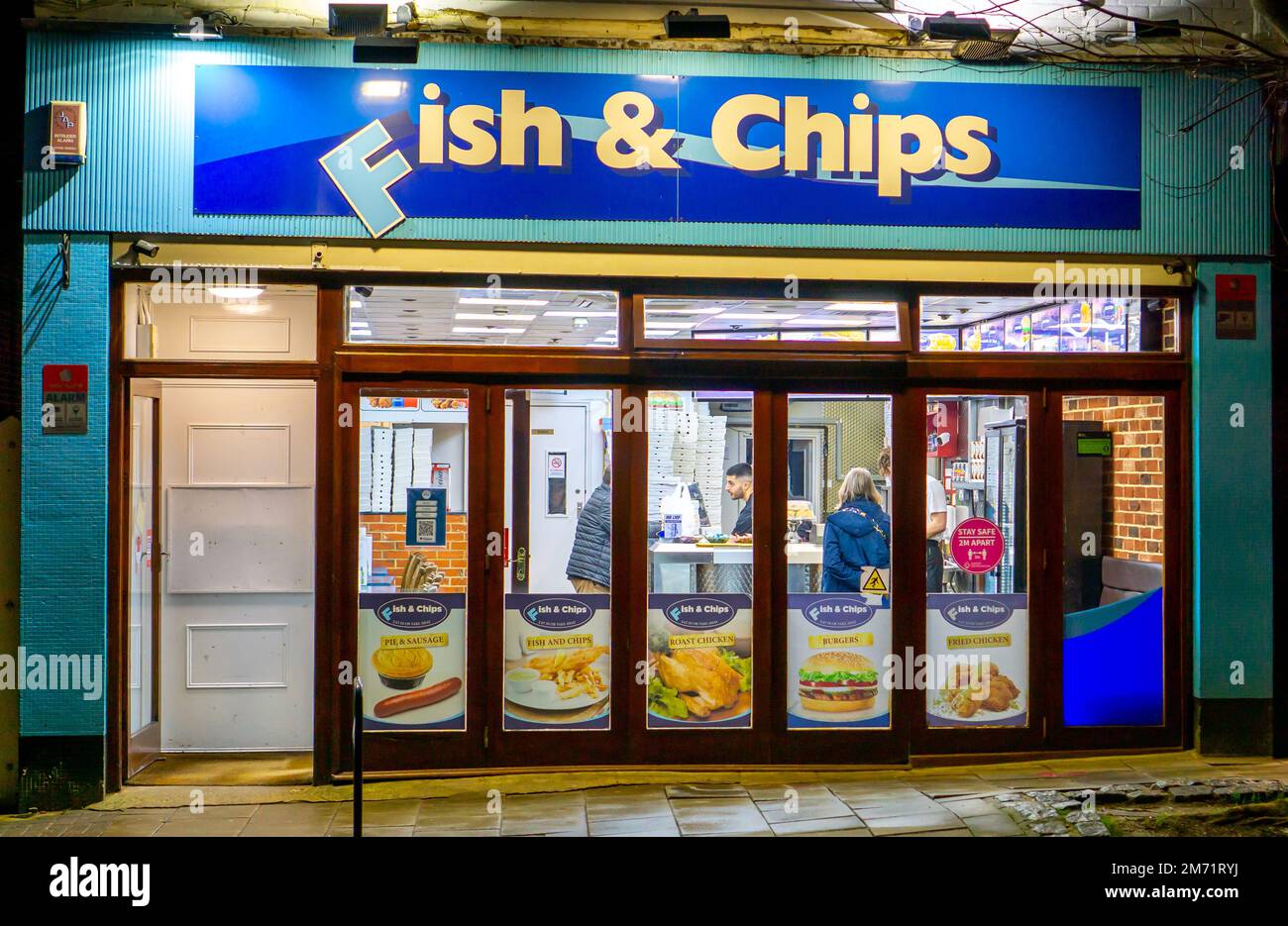 People inside a traditional British fish and chips shop lit up at night in Saffron Walden Stock