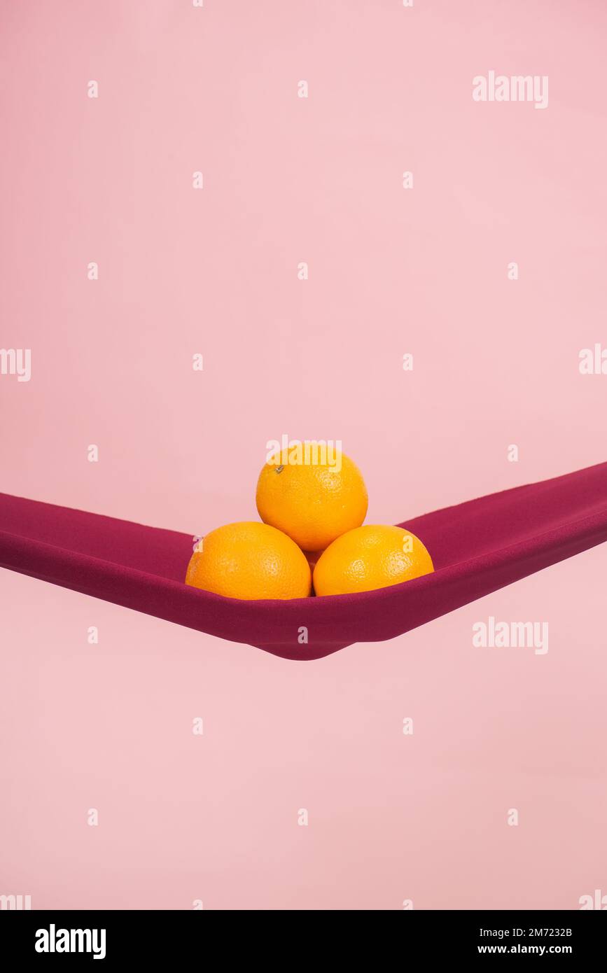four oranges cut in half on a red cloth in front of a peach background as a symbol of the pelvic floor, no people Stock Photo