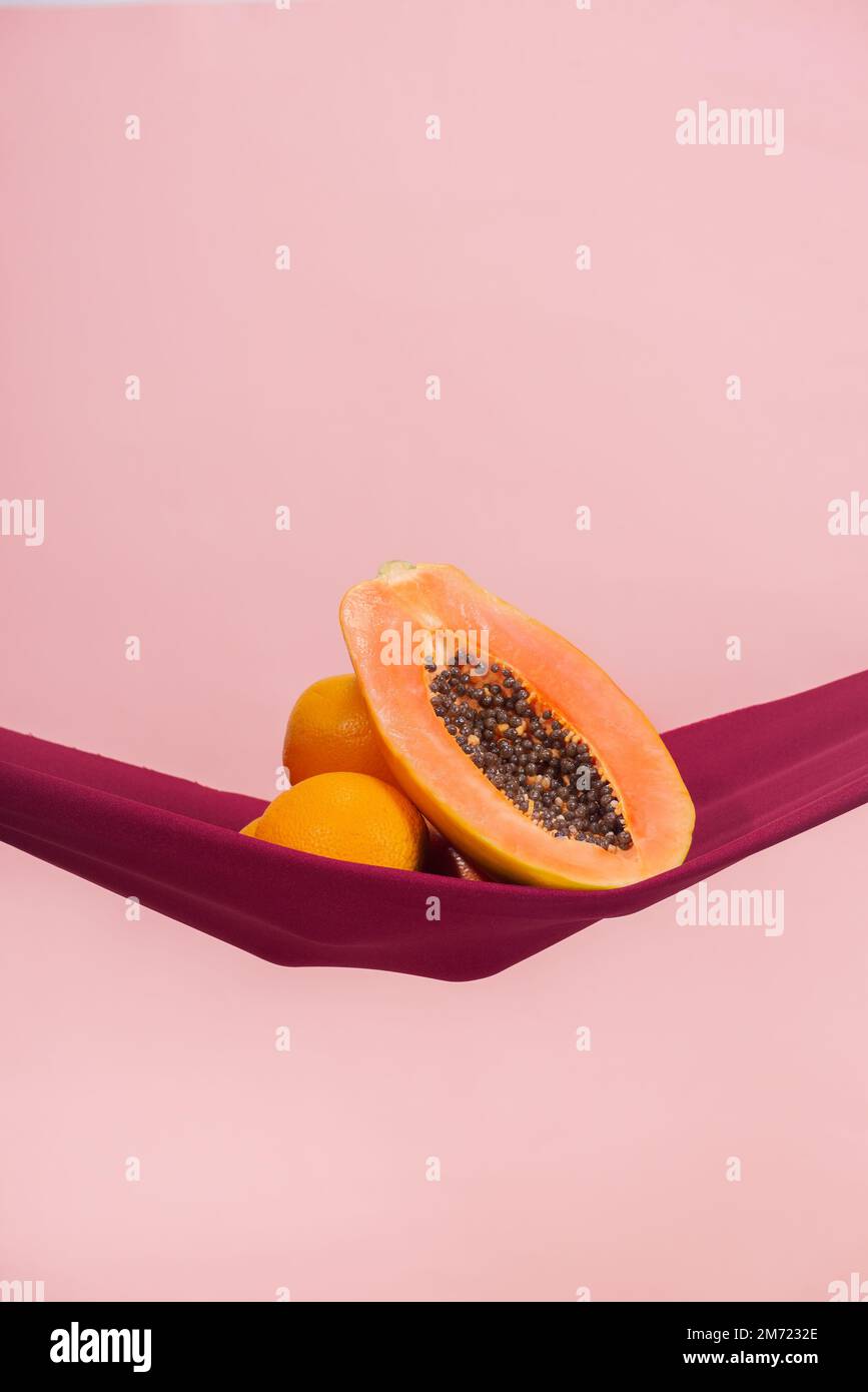 two oranges and a papaya cut in half on a red cloth in front of a peach background as a symbol of the pelvic floor, no people Stock Photo