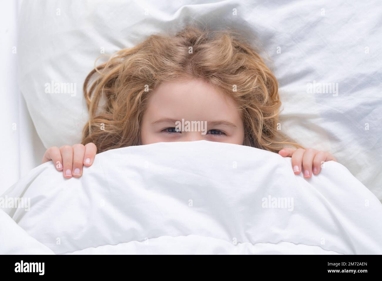 Kid under covers, face cover with blanket. Child wakes up in the morning in the bedroom. Cute
