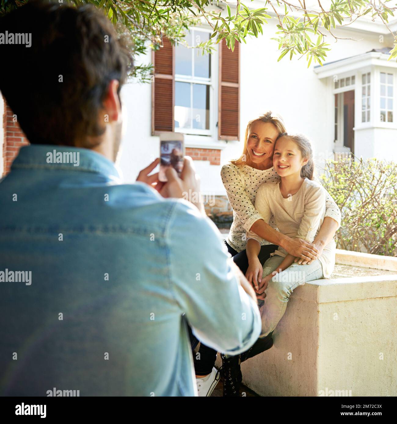 capture every moment. A man using his smartphone to take a photo of his family sitting outdoors. Stock Photo