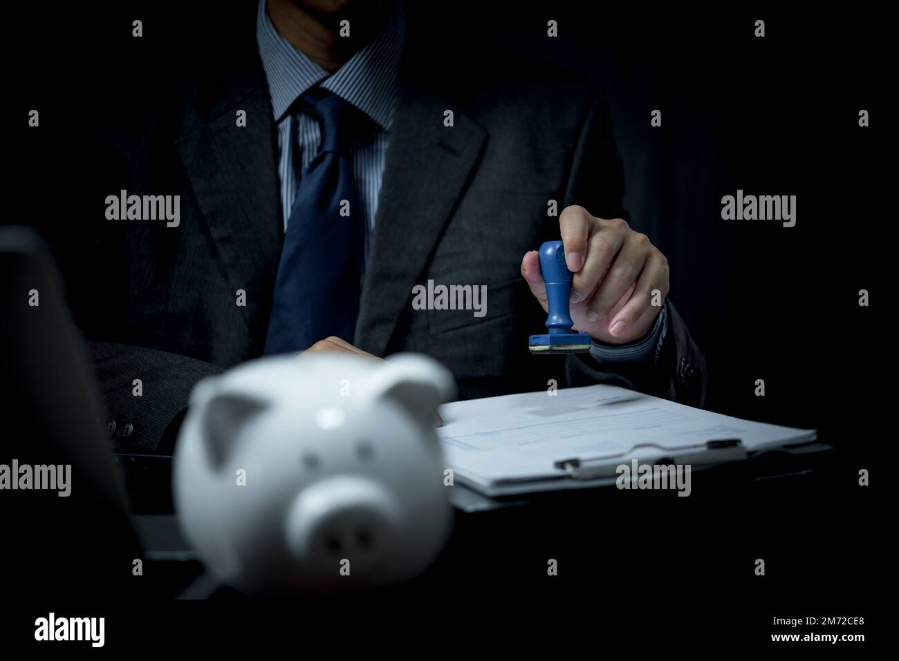 Businessperson is stamping a rubber stamp on a financial and banking approval document or paper contract agreement on desk. Stock Photo