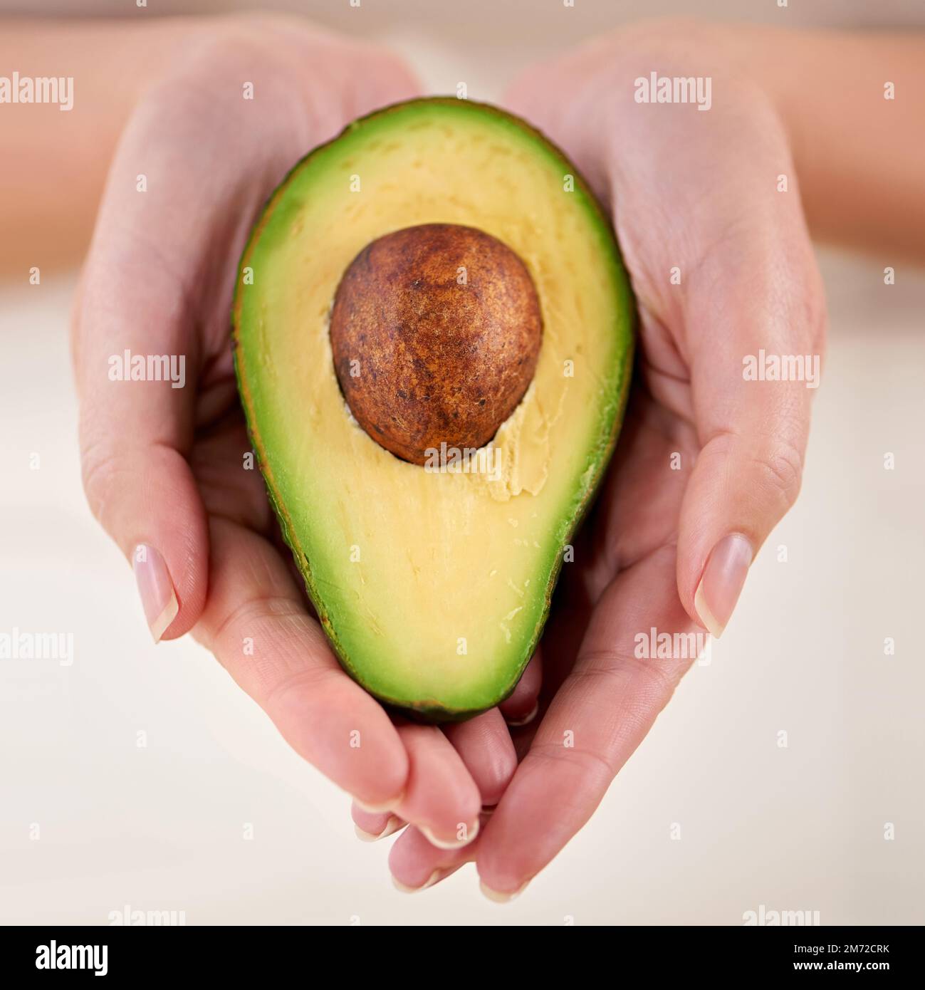 Good to eat and also great for your skin. a woman holding half an avocado in her cupped hands. Stock Photo