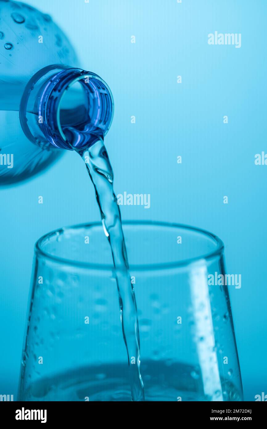 Water pouring from a plastic bottle into a glass beaker on a blue ...