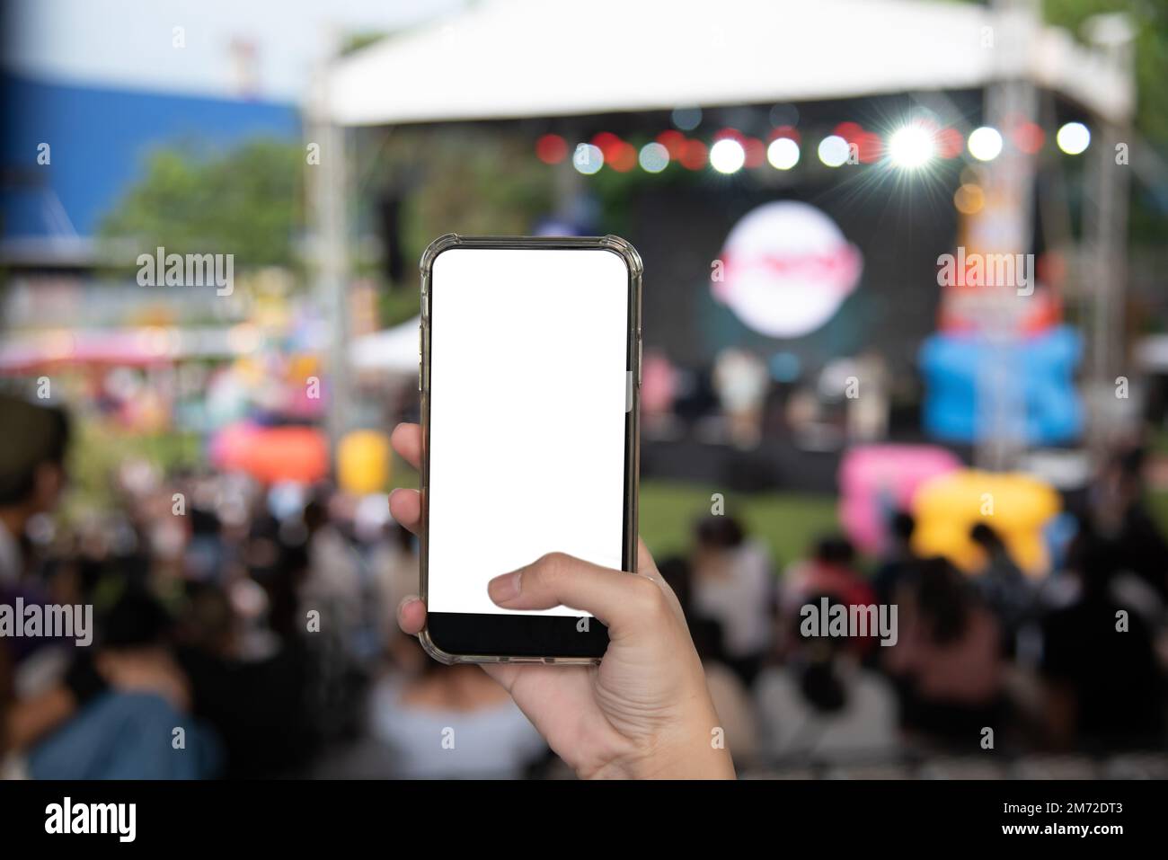 Hand holding mobile smartphone mock up white screen blank on music festival in the garden background. Stock Photo