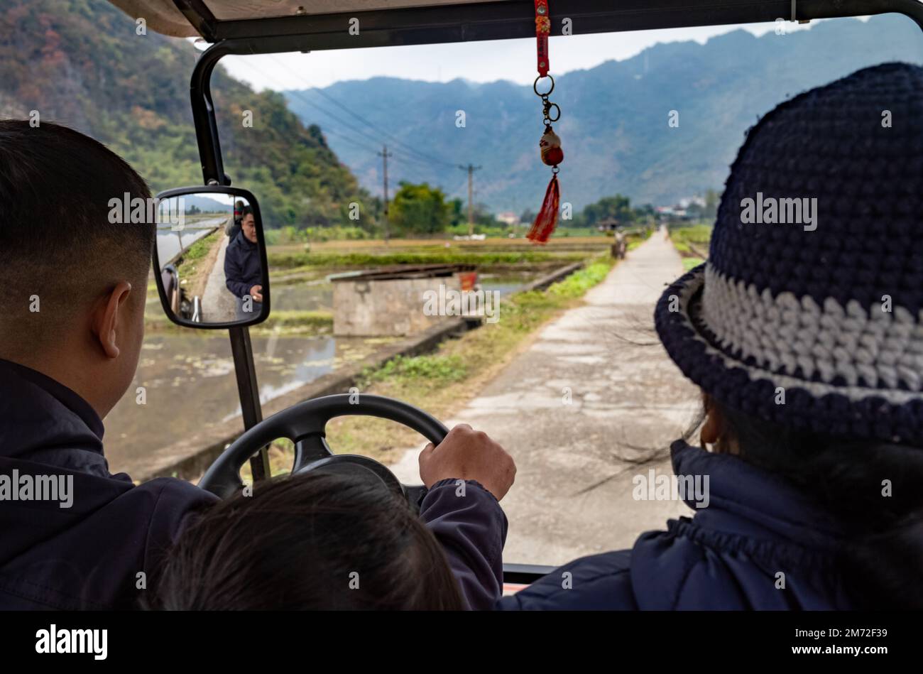A White Thai ethnic minority mother sits alongside her son as he drives an electric tourist car in Mai Chau, in the northern Vietnam highlands. Stock Photo
