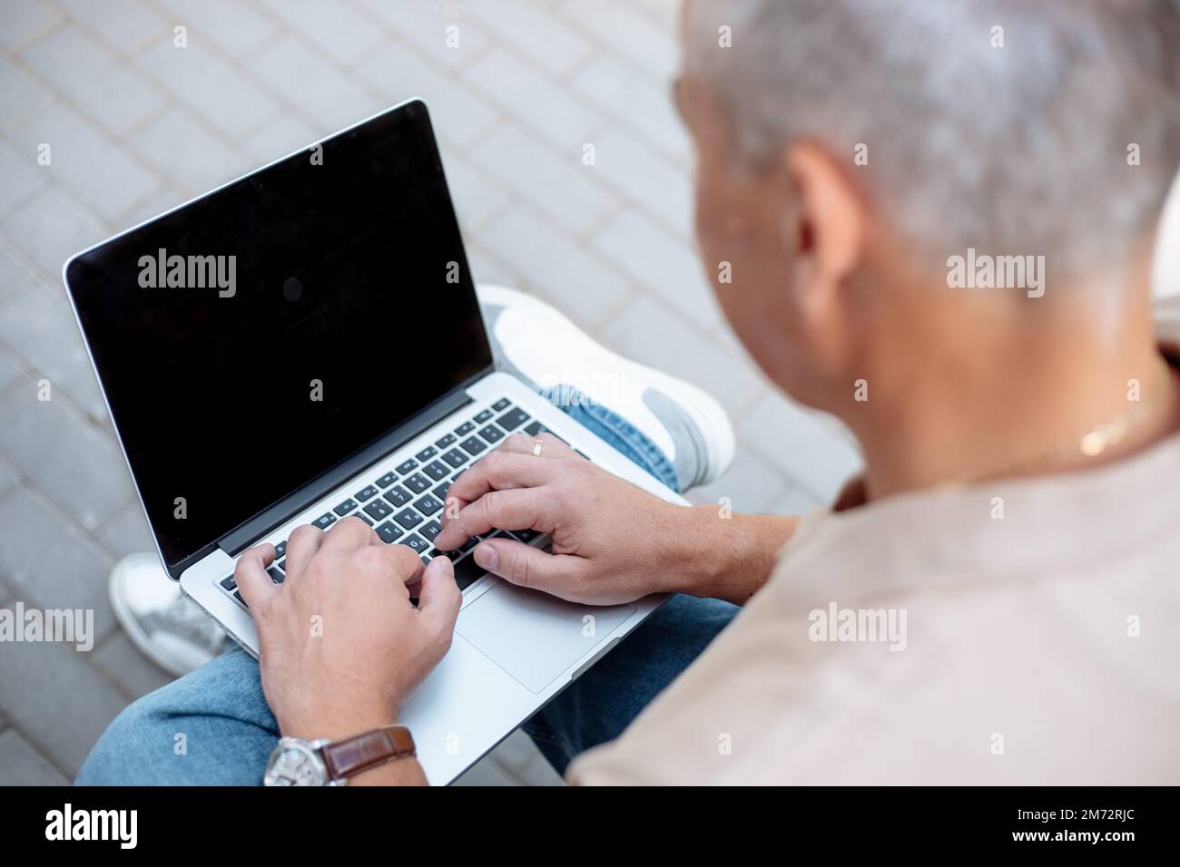 Unrecognizable gray haired businessman using laptop, black screen with place for advertisement text outdoors. IT job ad Stock Photo