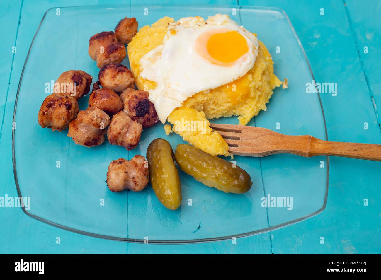Romanian traditional food, fried sausages, soft egg and 'mamaliga', side view close up, on blue background Stock Photo