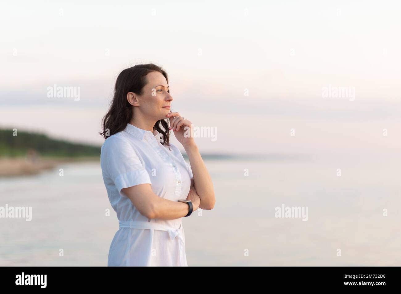 A mature woman stands on the beach and looks thoughtfully into the ...