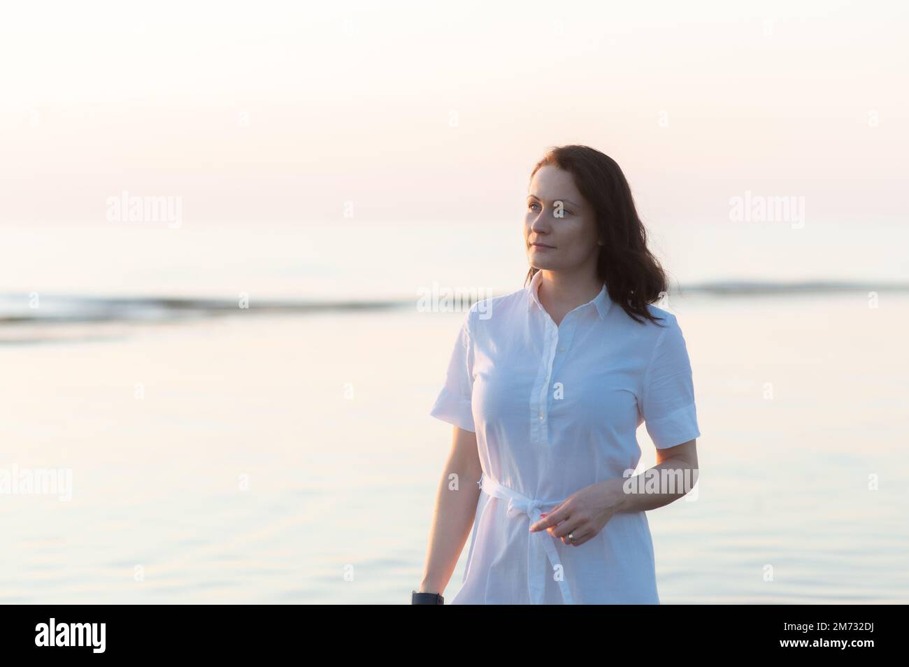 Pretty mature woman stands on the beach and looks thoughtfully into the ...