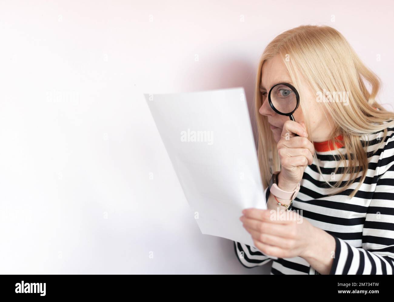 Funny mature woman standing isolated over light background, reading document with magnifying glass Stock Photo