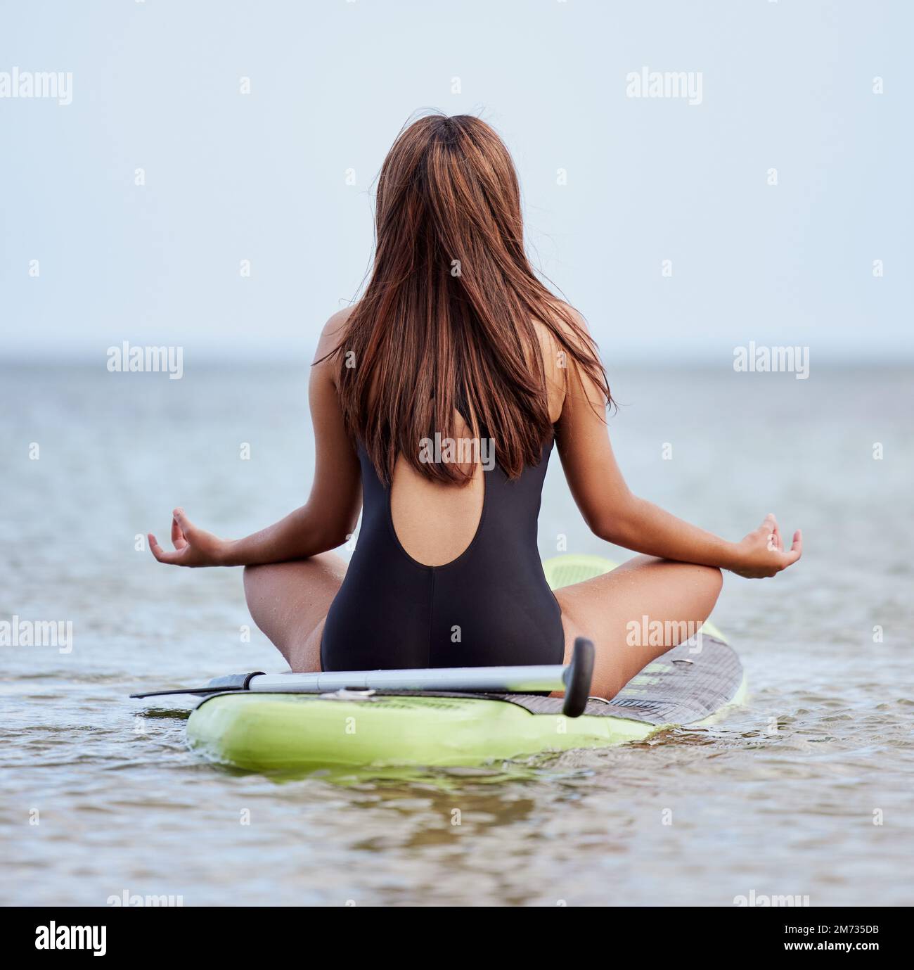 Girl in yoga pose with waves crashing over her legs on beach Stock