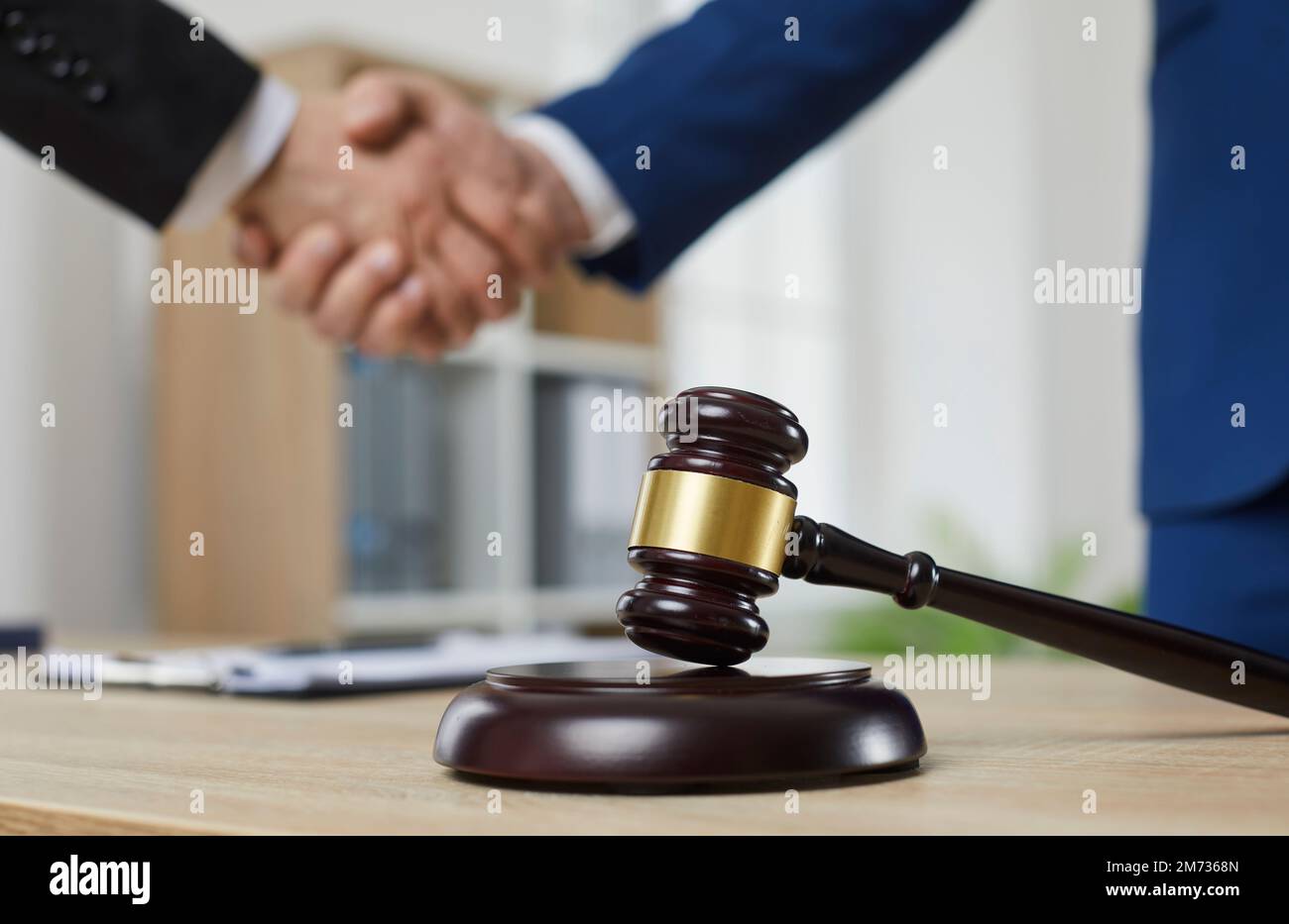 Close-up of a wooden court hammer on stand on table in the courtroom against the background of handshake. Stock Photo