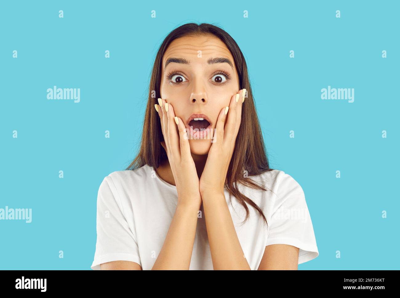 Woman holding her hands on face and looking at camera with shocked, scared expression Stock Photo