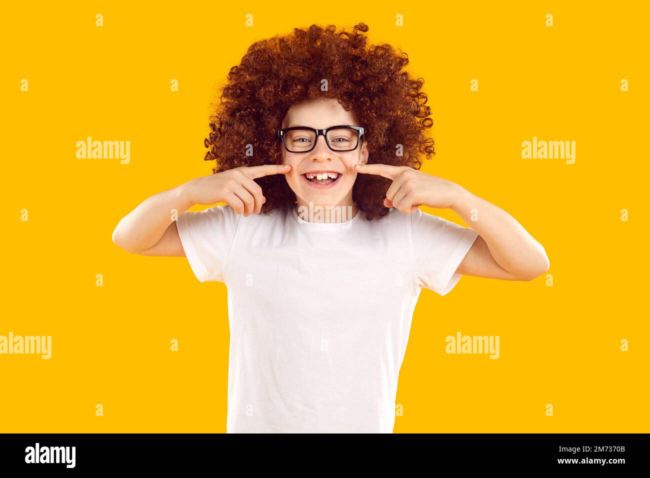 Funny happy joyful child in a curly wig showing his cheerful half toothless smile Stock Photo
