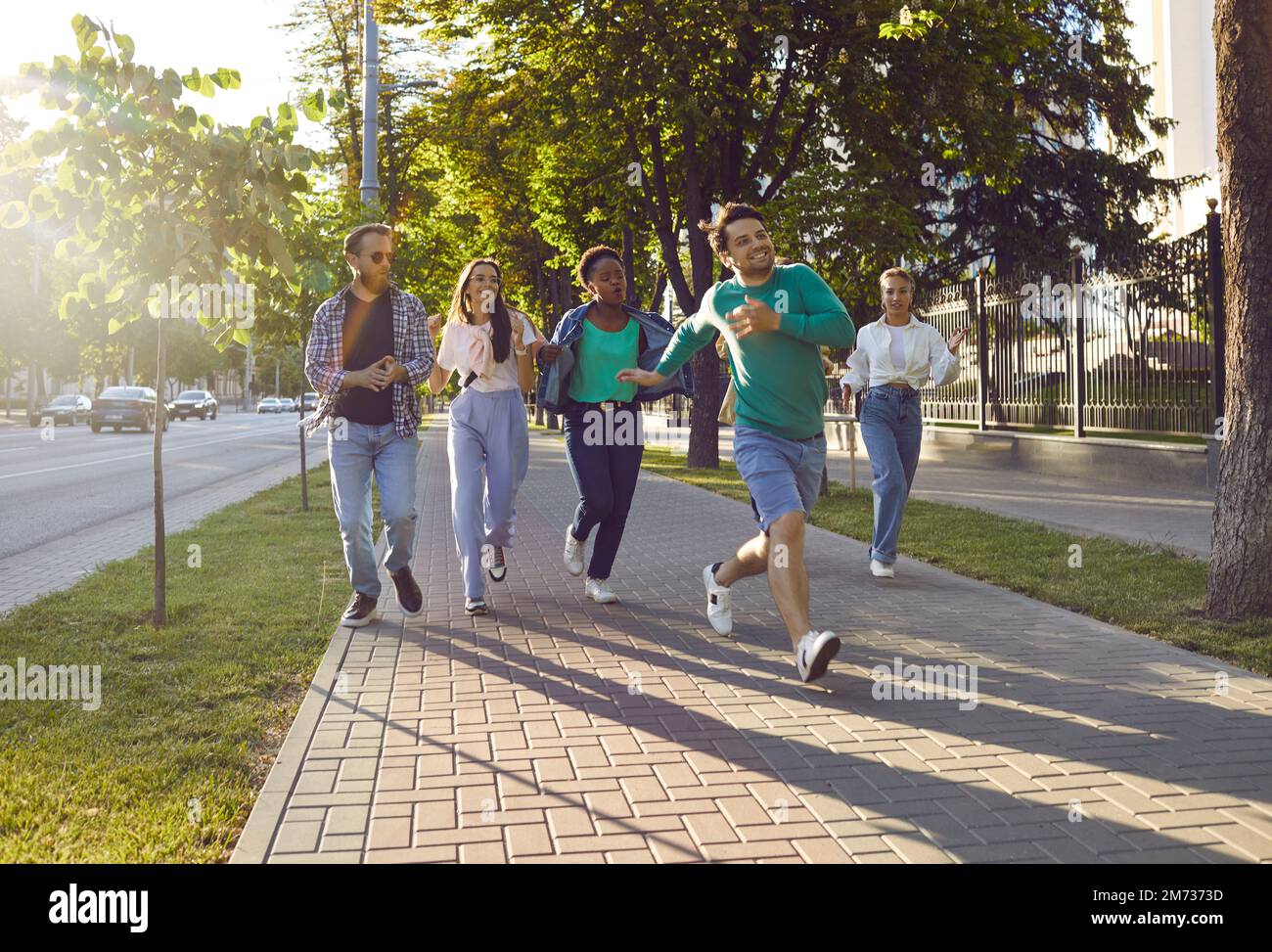 Happy multiethnic friends running on sidewalk while hanging out in summer city all together Stock Photo