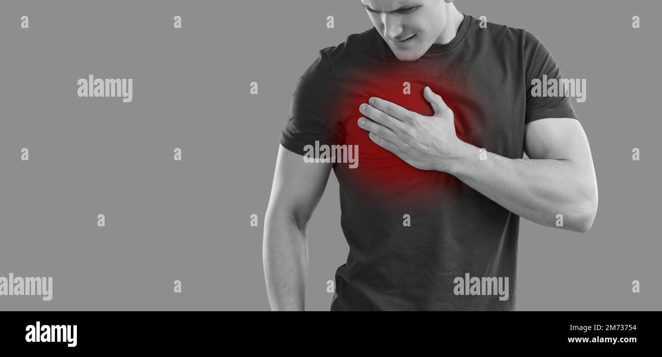 Young man has symptoms of burning in right side of chest while standing on gray background. Stock Photo