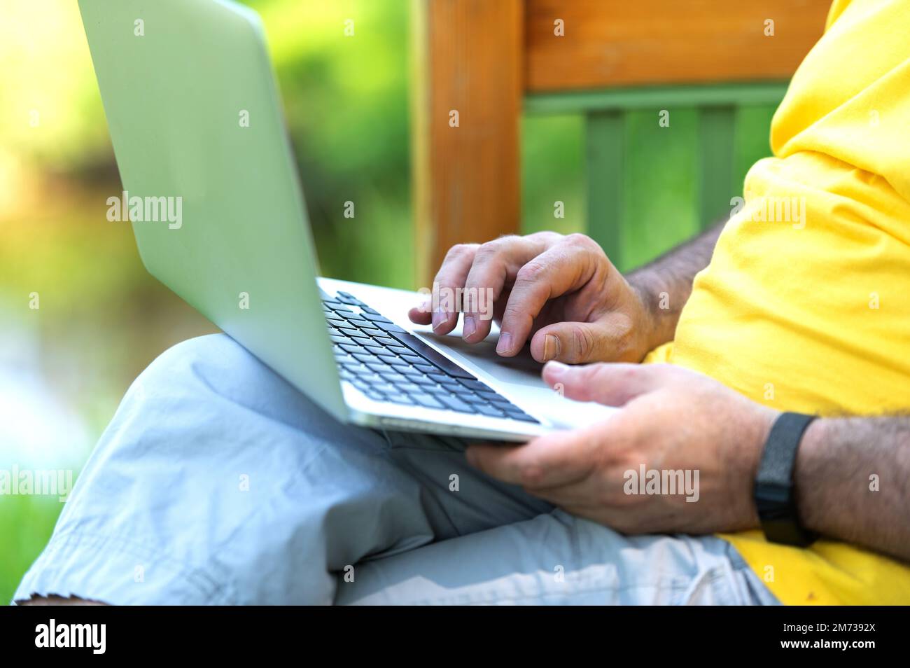A man working and typing on laptop keyboard while sitting in the park ...