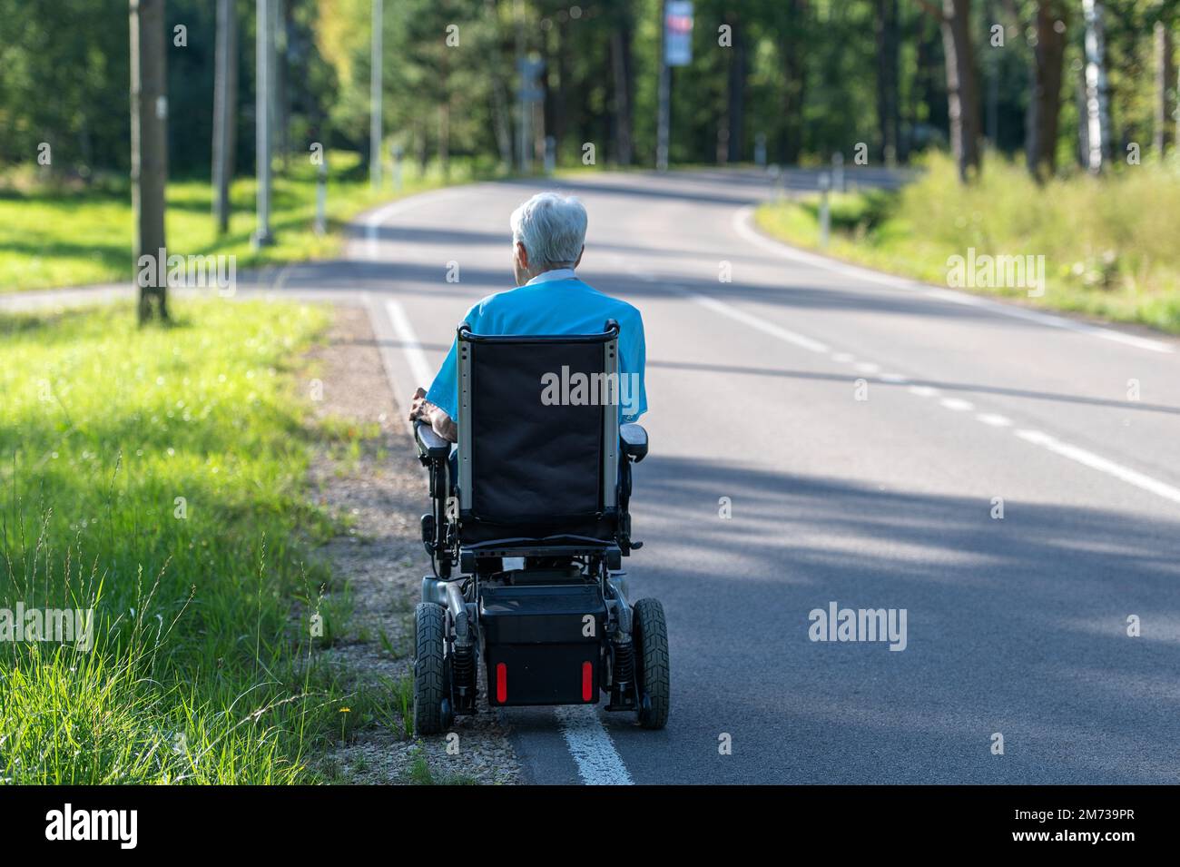Rear view on disabled old woman in a wheelchair on the highway Stock