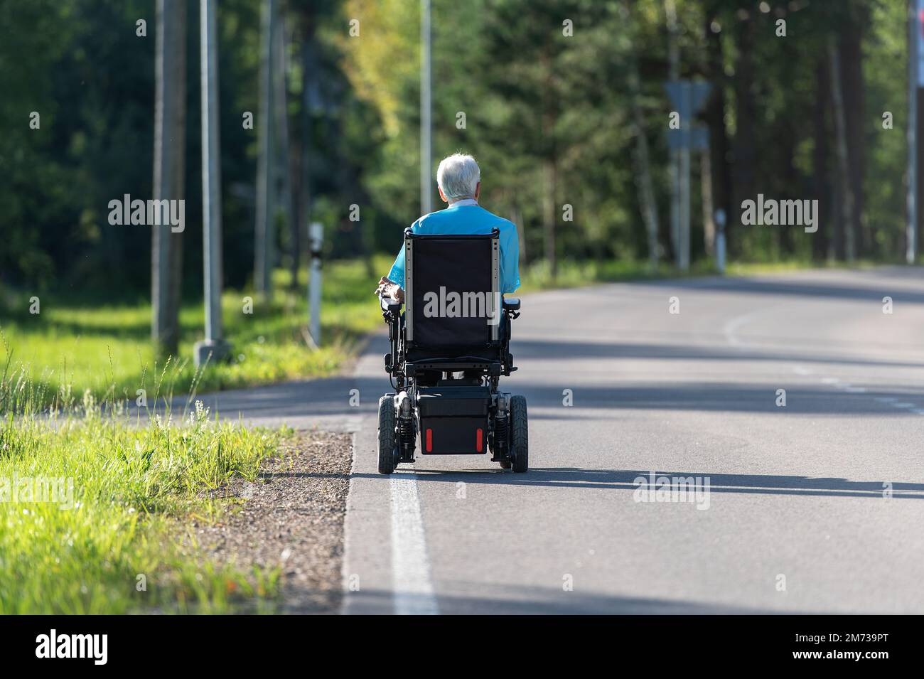 Rear view on disabled old woman in a wheelchair on the highway Stock
