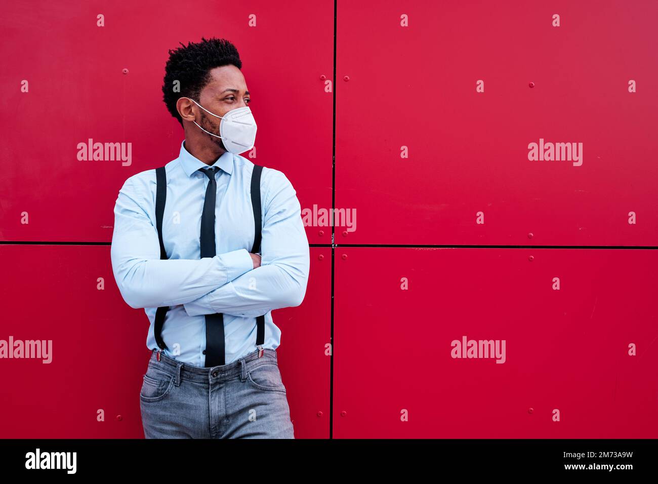 Businessman with face mask looking away while standing with arms crossed outdoors. Stock Photo