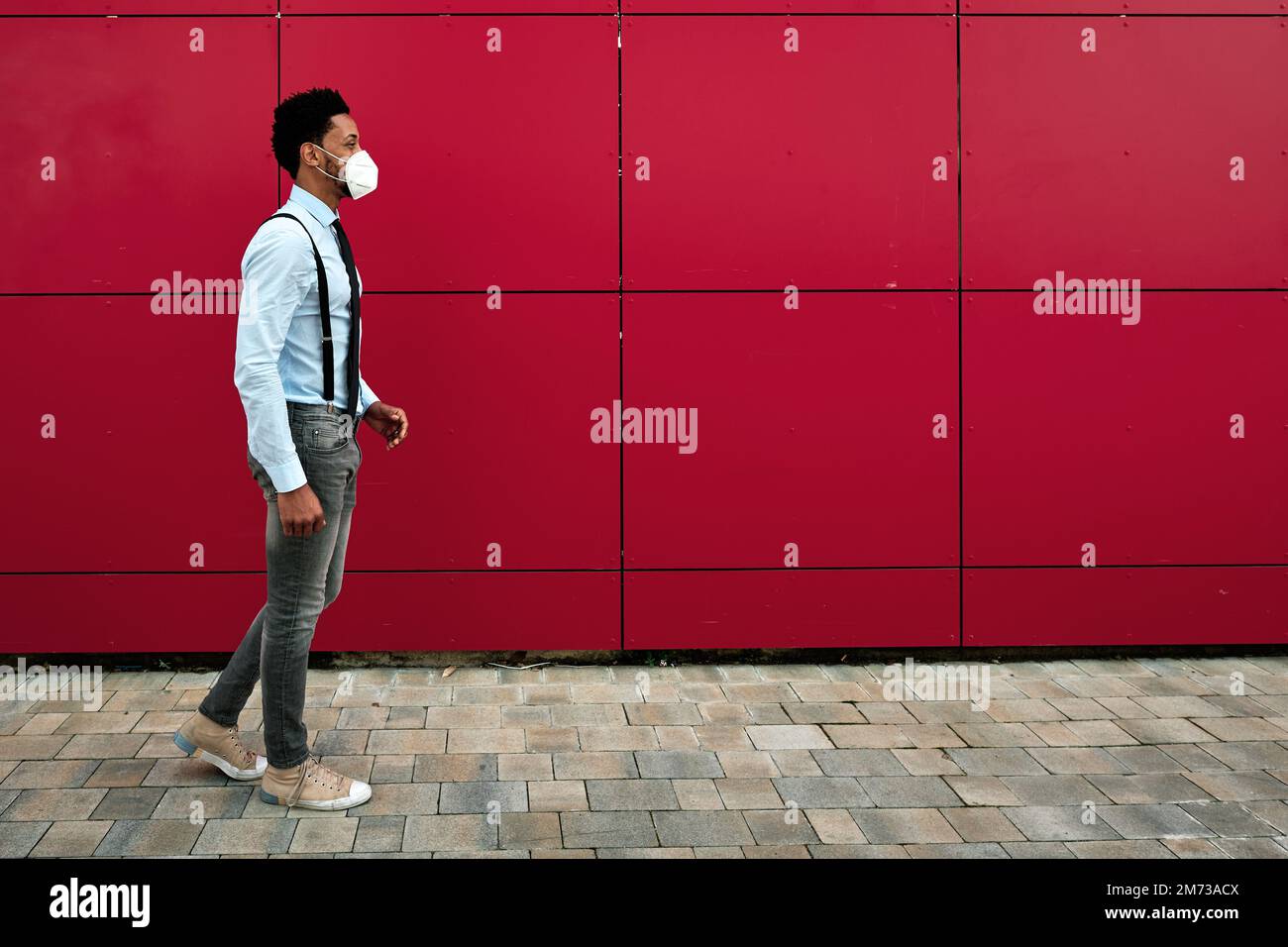 Man with face mask walking outdoors on the street. Stock Photo