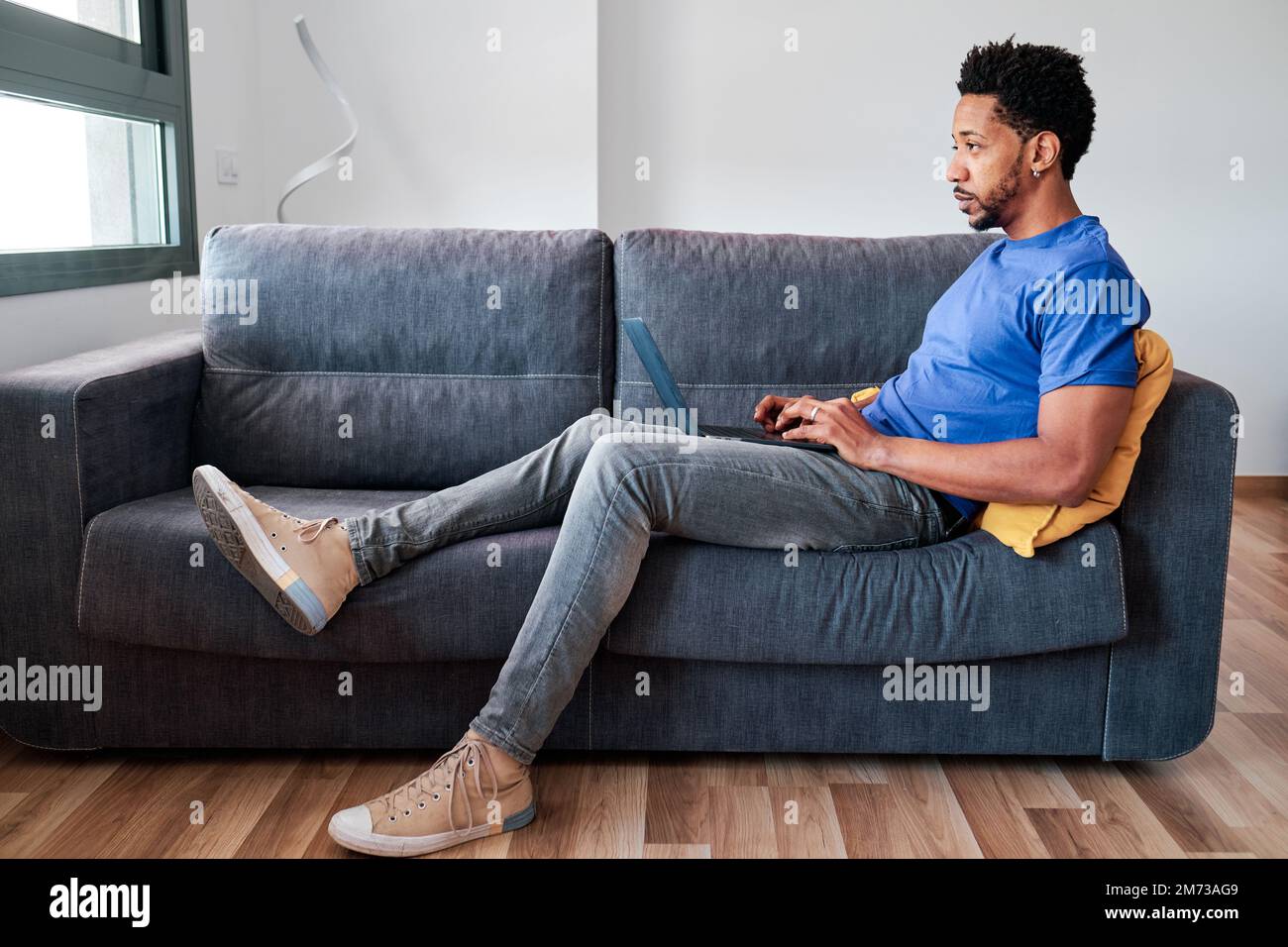 Man using a laptop while sitting on a sofa at home. Stock Photo