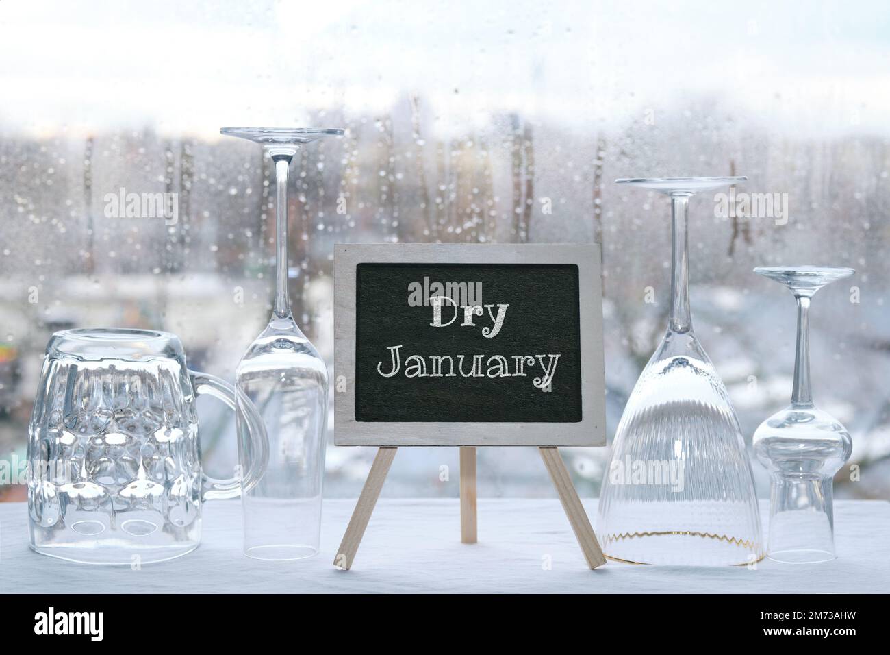 Dry January, month without alcohol. Chalk text, caption Dry January on blackboard, chalk board. Empty vine and beer drinking glasses. Window with rain Stock Photo