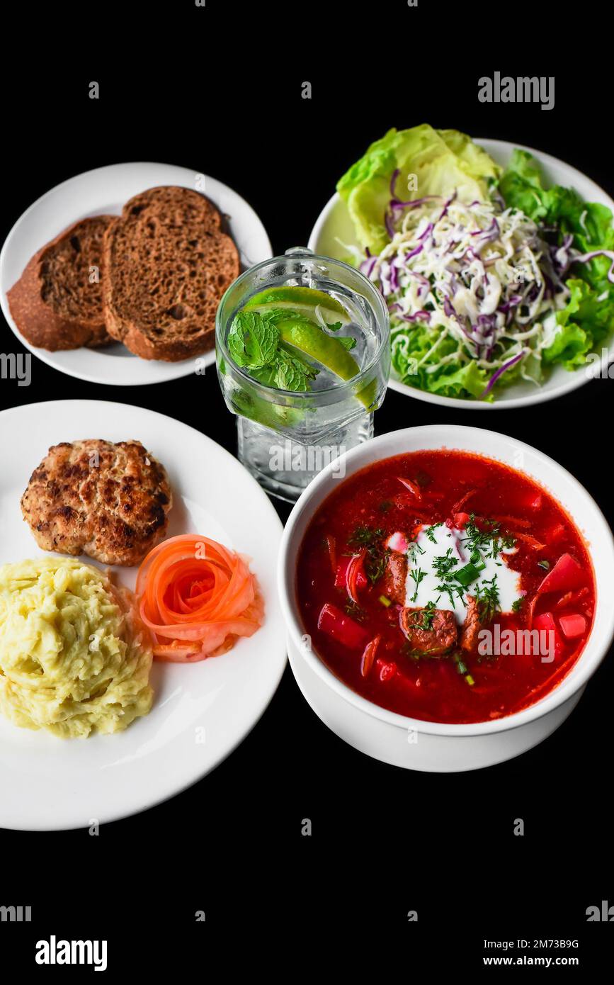 Combo set with borscht, mashed potato, black bread, salad on black background top view Stock Photo