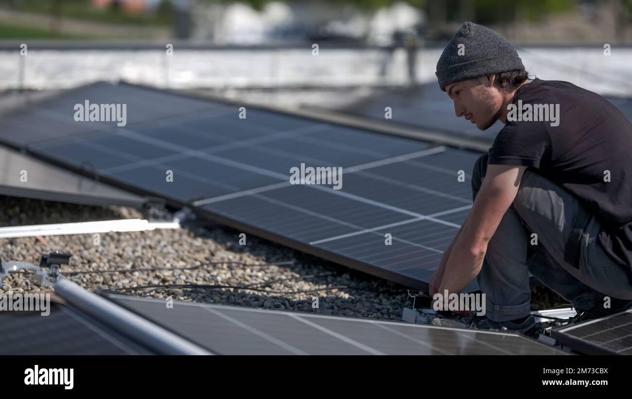 Male team engineers installing stand-alone solar photovoltaic panel system. Electricians mounting blue solar module on roof of company roof. Alternati Stock Photo