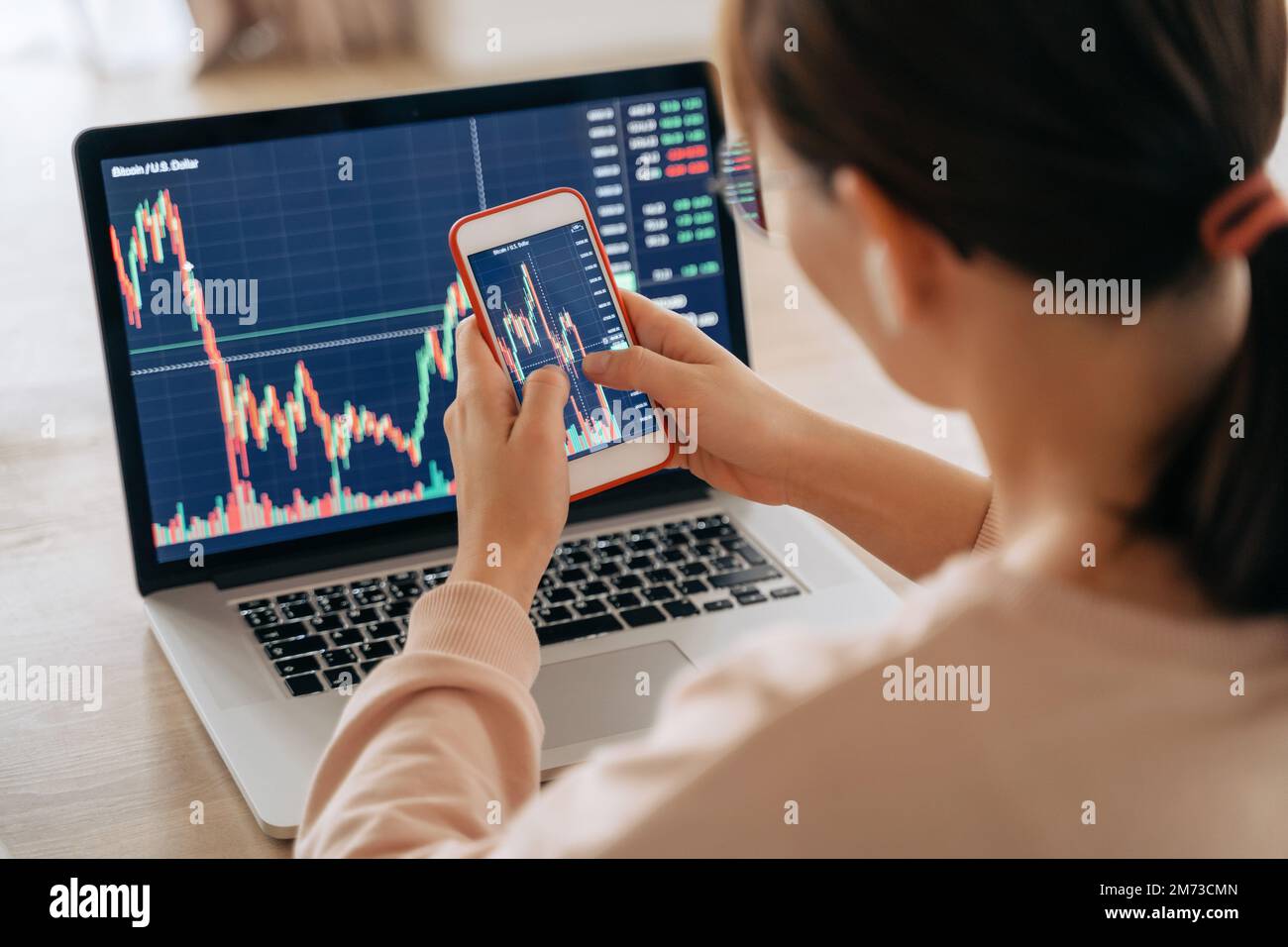 Woman crypto trader investor broker using smartphone app and laptop executing financial stock trade market trading order to buy or sell cryptocurrency. Selective focus on hands and cellphone screen Stock Photo