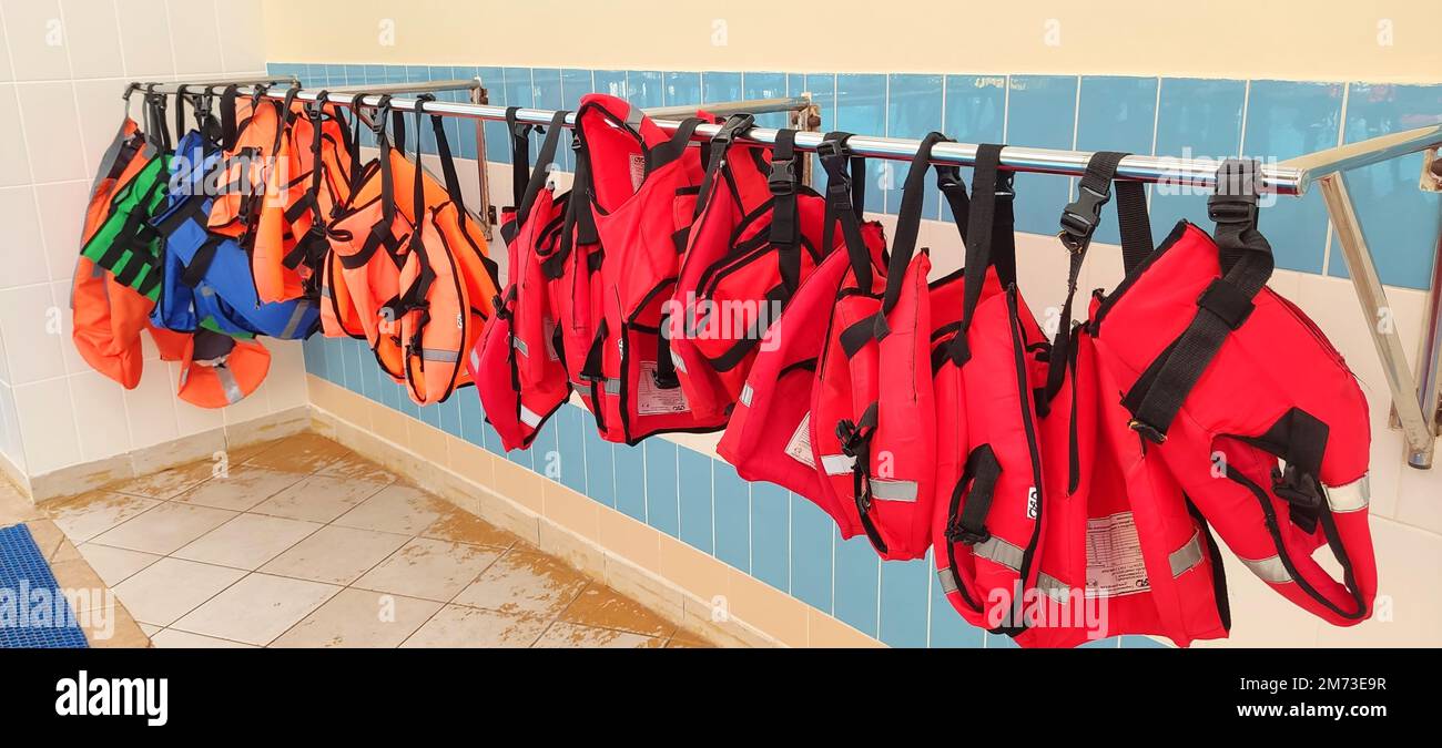 Several red and orange life jackets hang on a hanger, near the gouboi