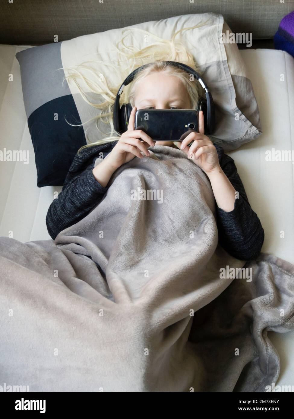 A teenage boy is lying in his bed listening to music from his smartphone. Seen from directly above. Stock Photo