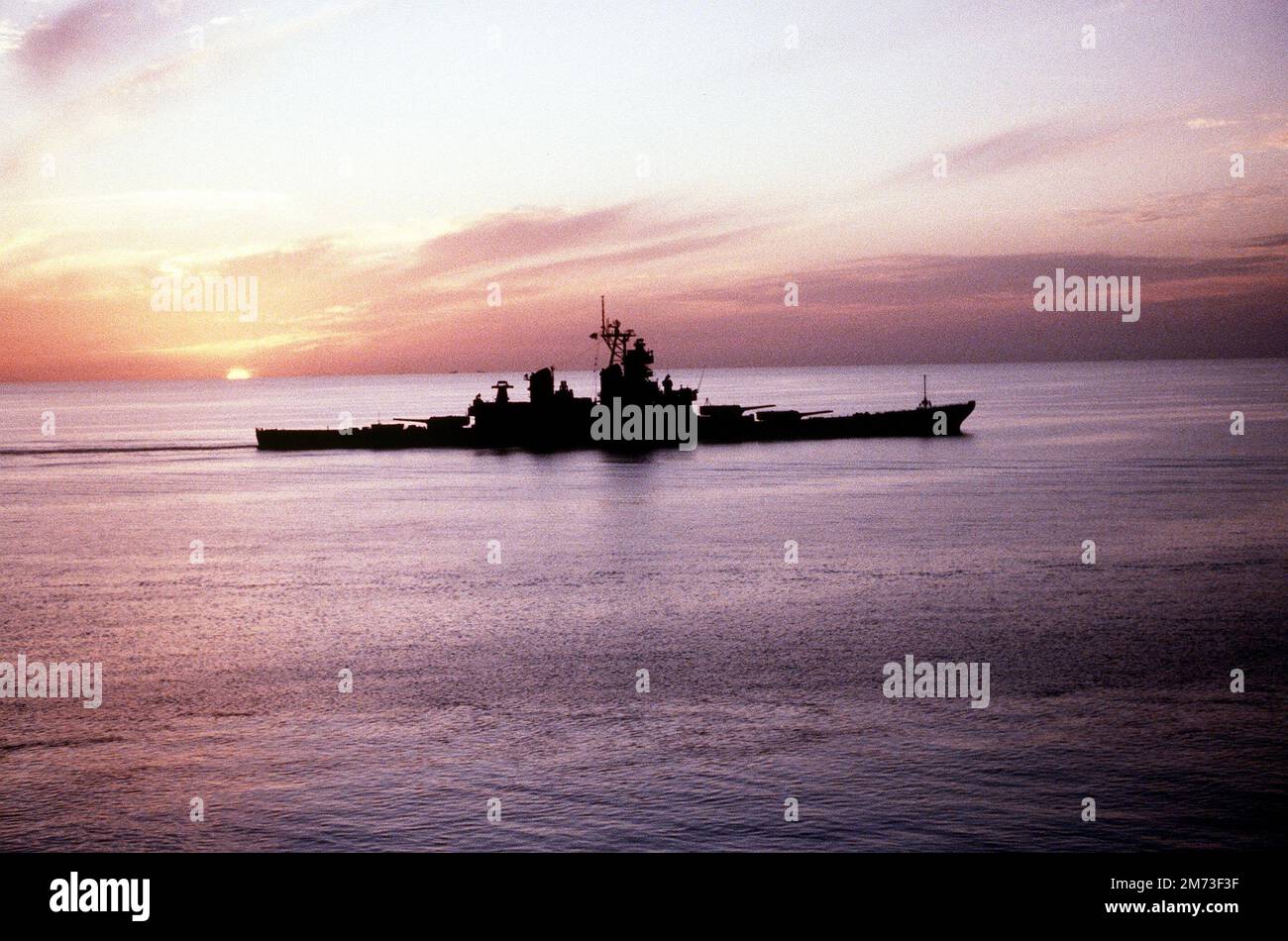 The setting sun silhouettes the battleship USS MISSOURI (BB-63). Stock Photo