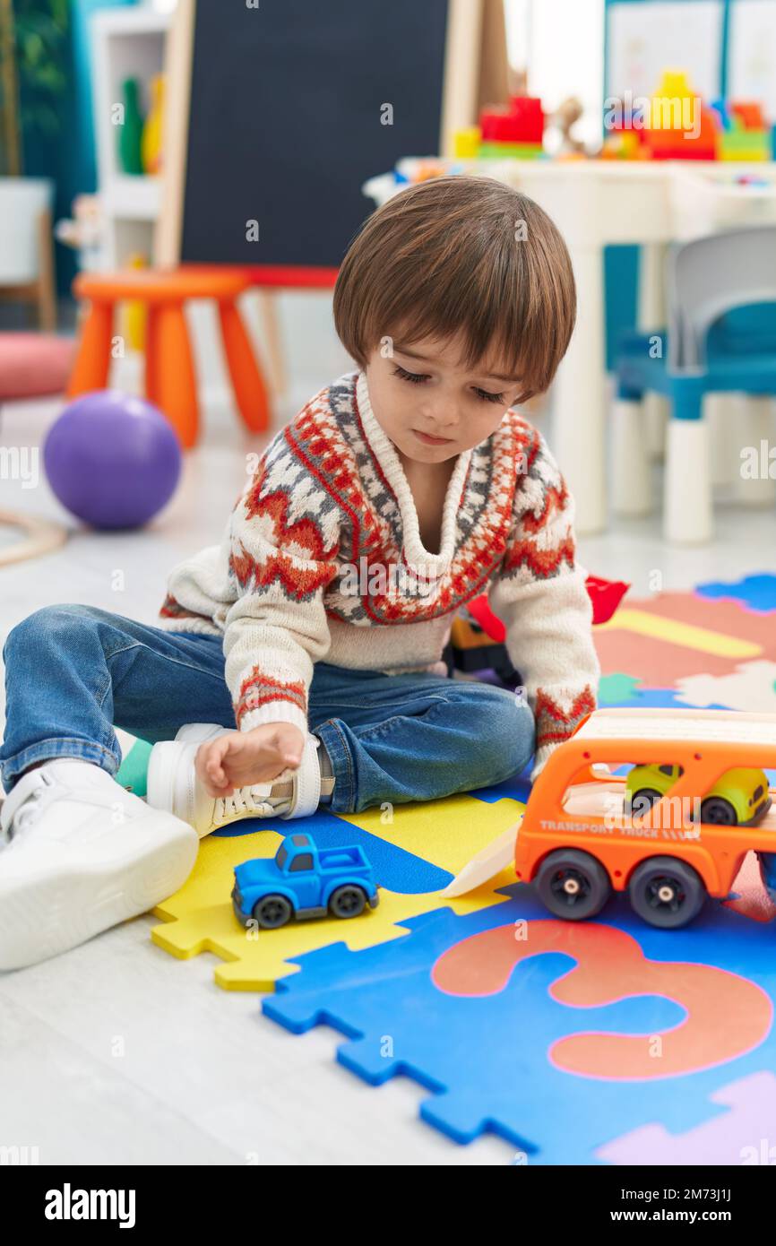 Adorable toddler playing with car toy sitting on floor at kindergarten ...