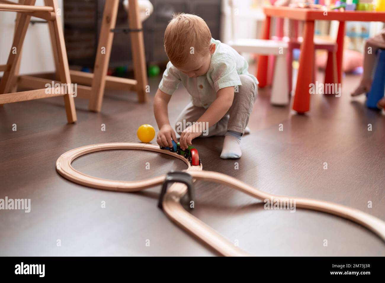 Adorable toddler playing with cars toy sitting on floor at kindergarten ...