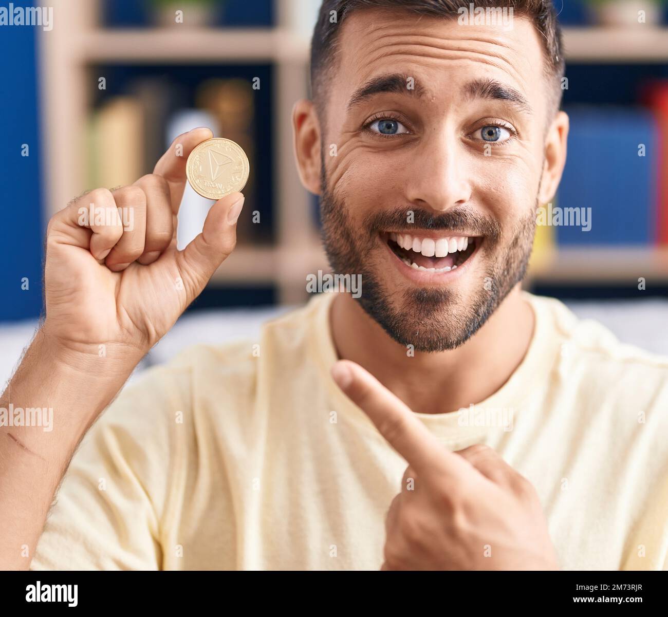 Handsome hispanic man holding tron cryptocurrency coin smiling happy  pointing with hand and finger Stock Photo - Alamy
