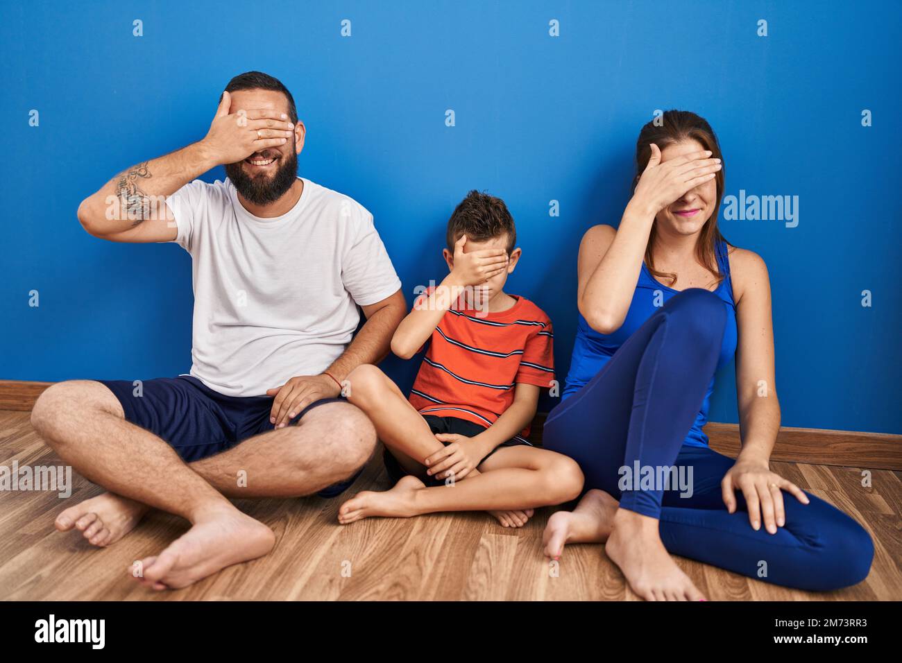 Family of three sitting on the floor at home smiling and laughing with ...
