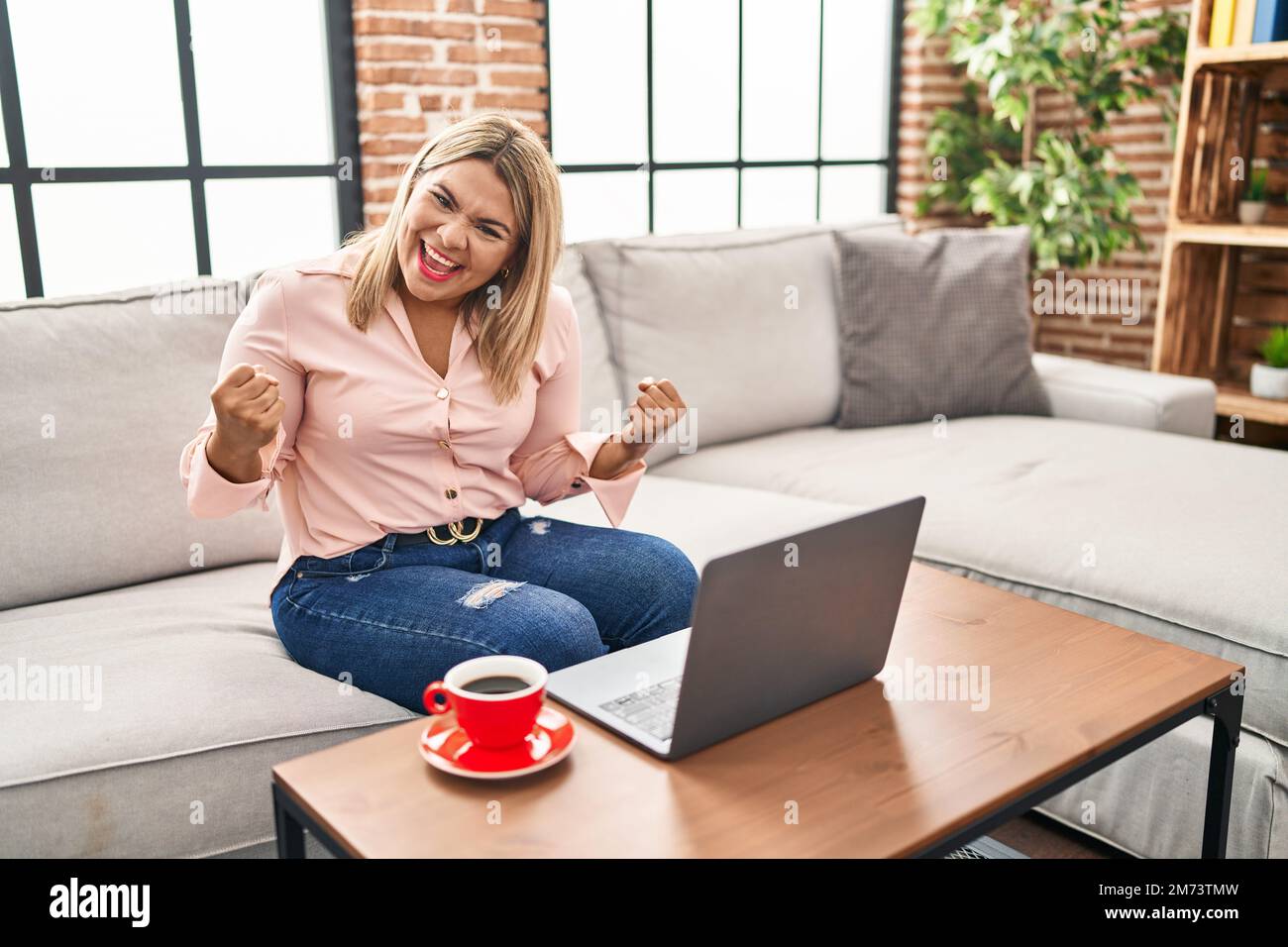 Young hispanic woman using laptop sitting on the sofa at home very ...