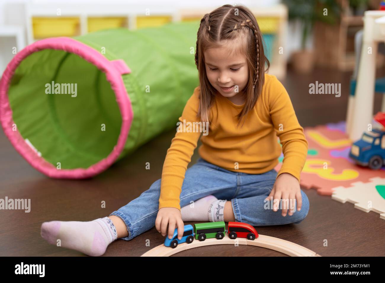 Adorable hispanic girl playing with cars toy sitting on floor at ...
