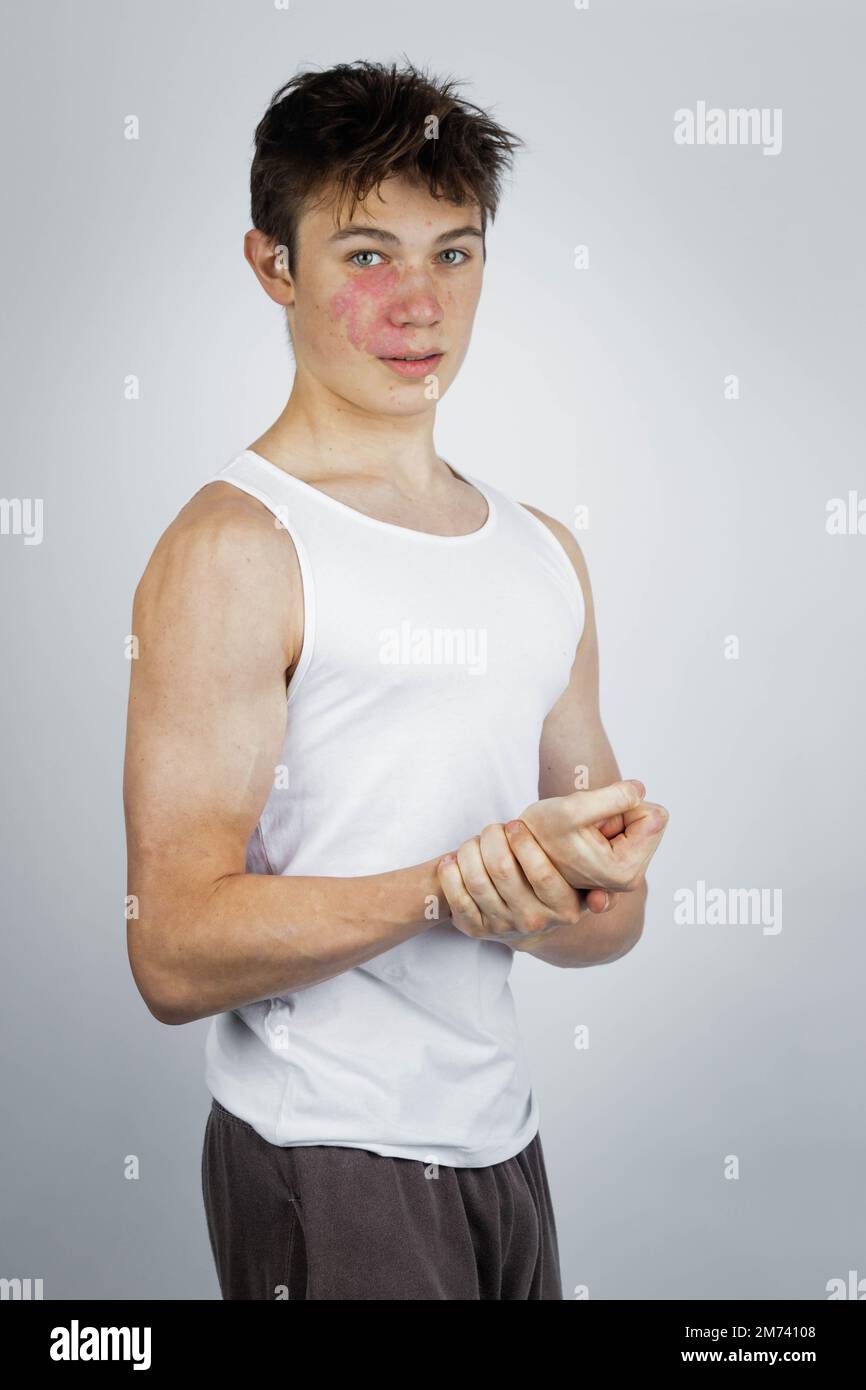 A 17 year old teenage boy wearing a white tank top flexing his arm