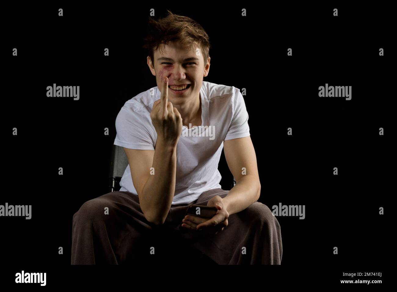 Sitting 17 year old teen boy making a rude gesture with his middle