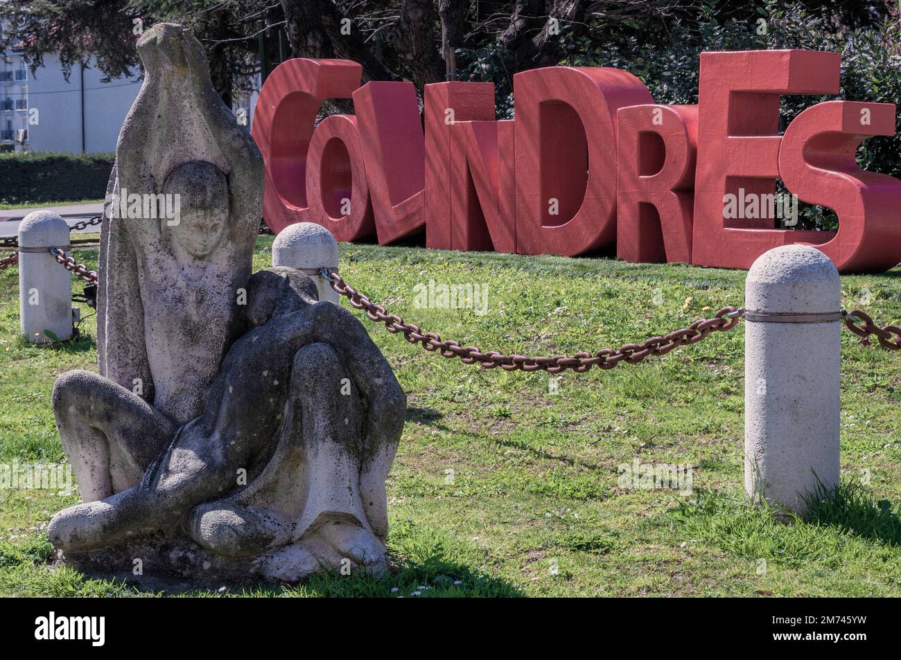 Modern sculpture of La piedad, made of limestone with the name in red letters of the town of Colindres in the background, Cantabria, Spain. Stock Photo