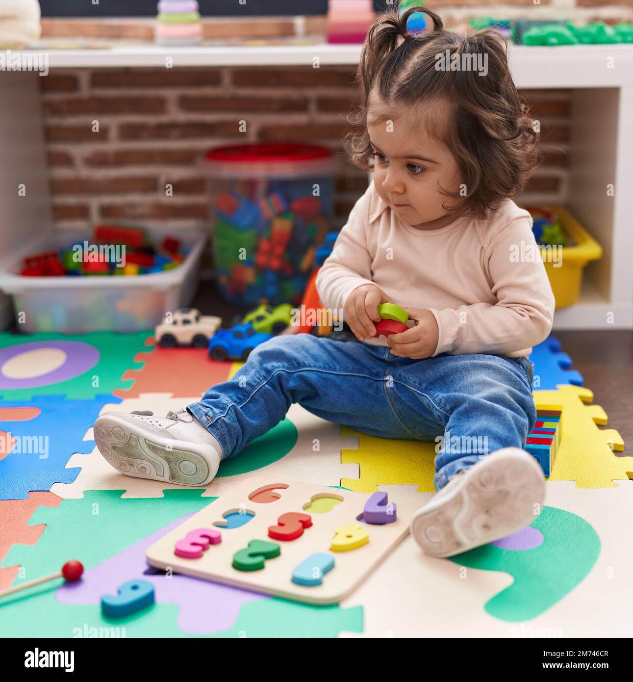 Adorable hispanic girl playing with maths puzzle game sitting on floor ...