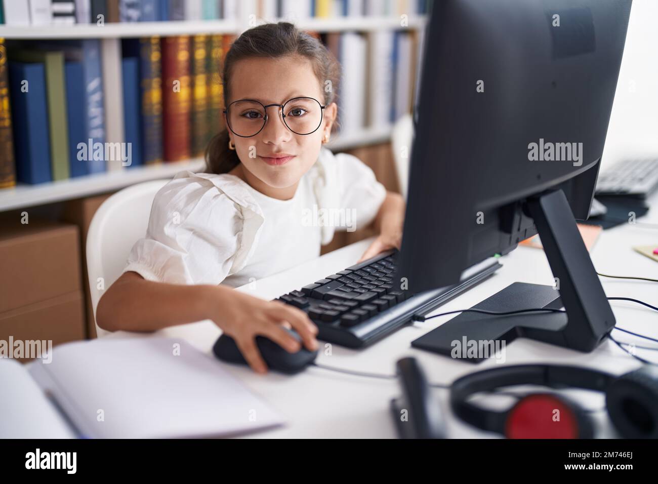 Adorable hispanic girl student using computer sitting on table at ...